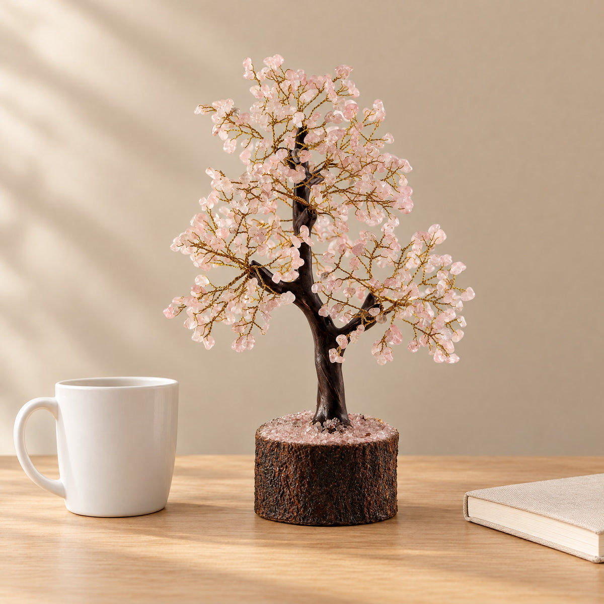 Rose quartz crystal tree on a desk beside a coffee mug for size