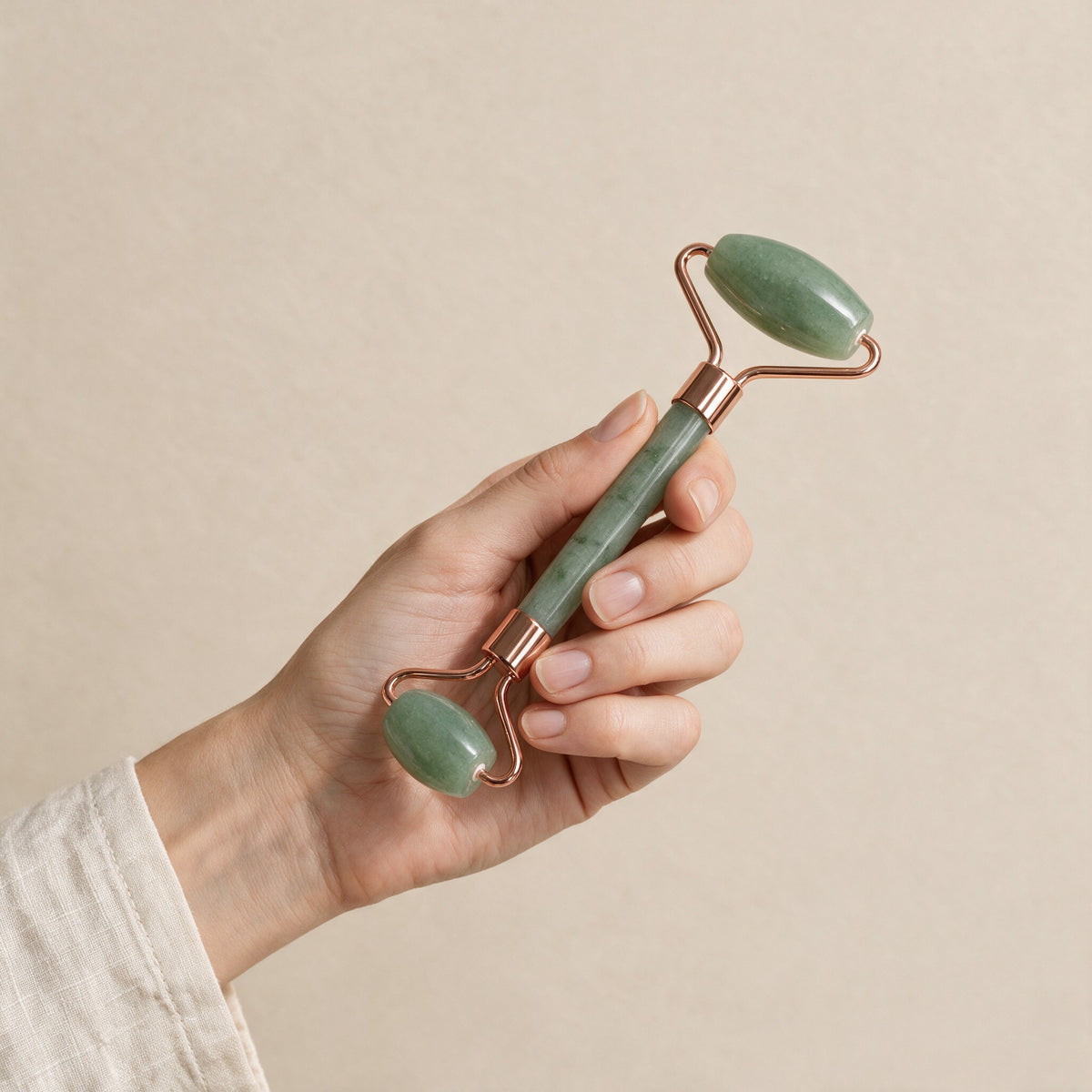 Green jade face roller with rose-gold-tone frame held in a hand for size