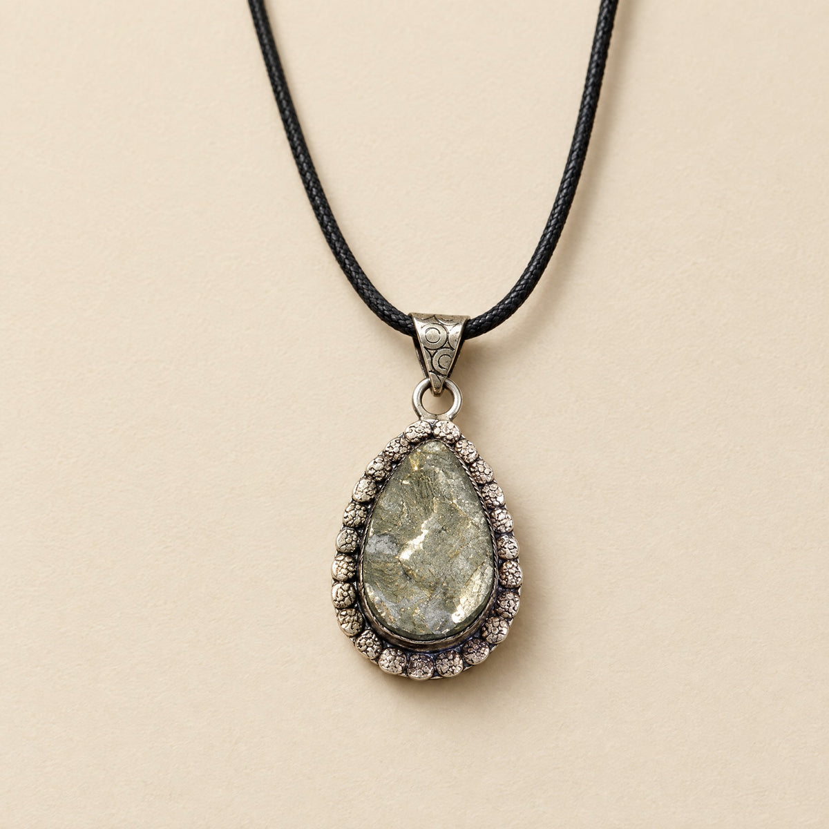 Pyrite teardrop pendant in an ornate silver-tone frame on black cord